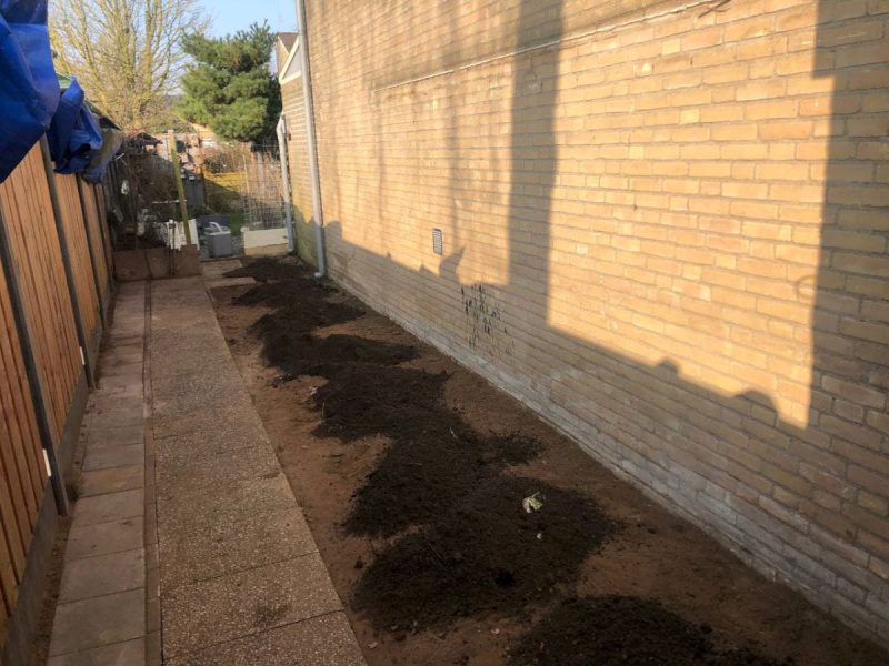 Naast een bakstenen muur wordt een tuin uitgegraven.