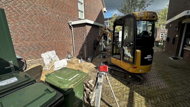 Voor een huis staat een graafmachine geparkeerd.