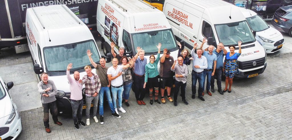 Een team dat voor een groep busjes staat en een foto maakt ter herdenking van hun duurzame funderingsherstelproject.