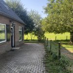 Een bakstenen huis midden in een veld met een erf.