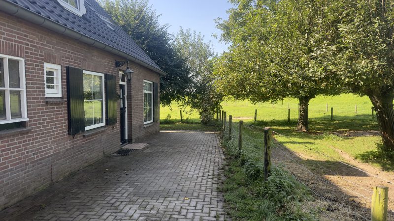 Een bakstenen huis midden in een veld met een erf.