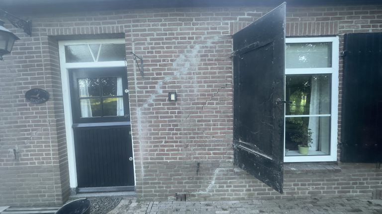 Een bakstenen huis met zwarte luiken en een deur.