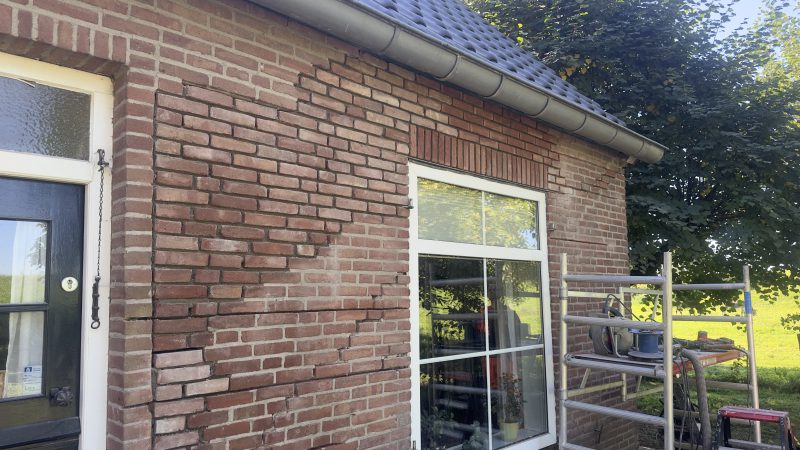 Een gemetselde muur van een huis met een ladder ervoor.