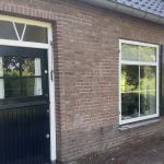 Een bakstenen huis midden in een veld met een erf.