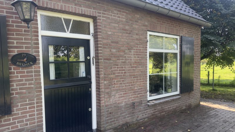 Een huis met een zwarte deur en zwarte luiken en een muur waar voegwerk recent is aangebracht.