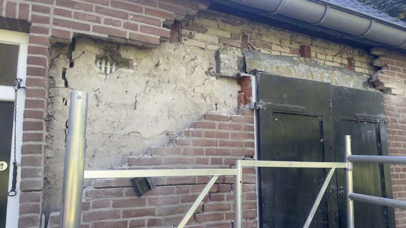 Een huis met een bakstenen muur waar stenen zijn verwijderd en een ladder.